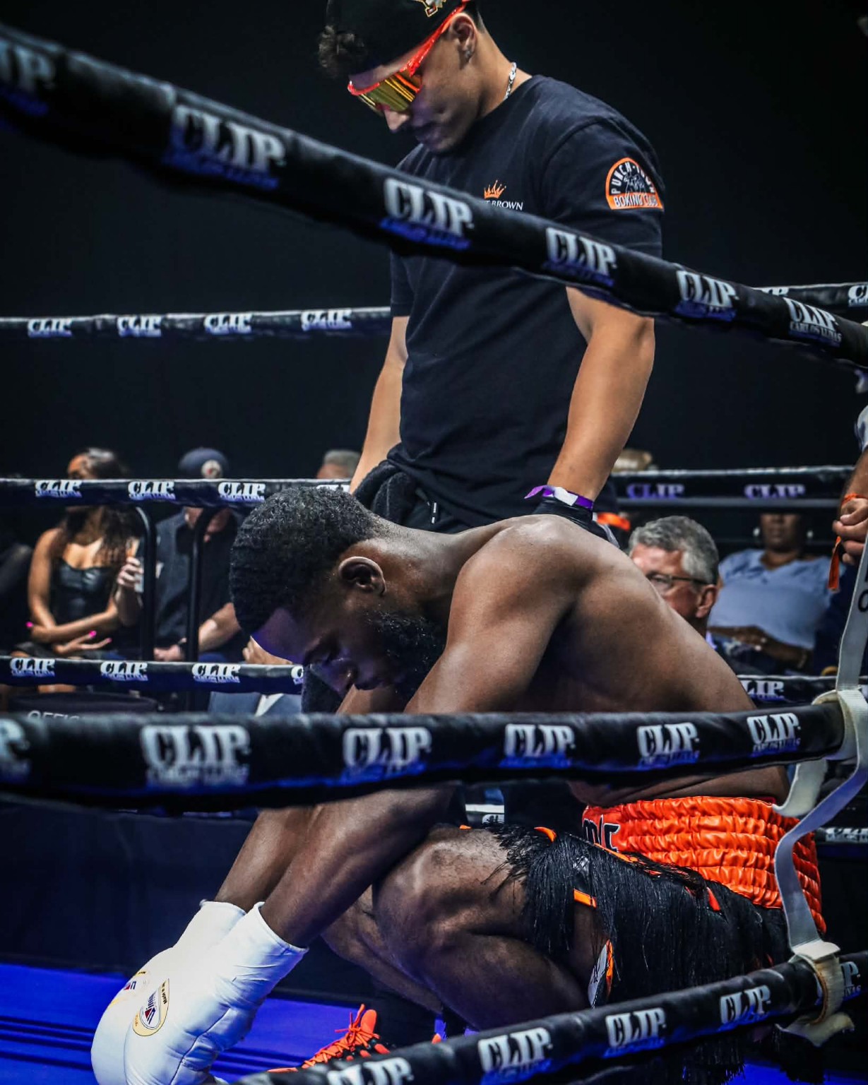 A PunchTown boxer leaning on the ropes between rounds while his cornerman stands behind him