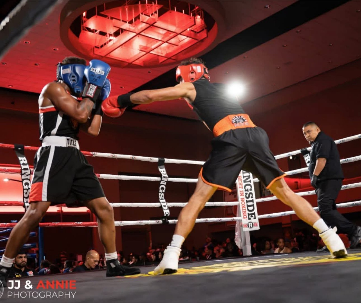 Two amateur boxers compete in ring action with a referee nearby