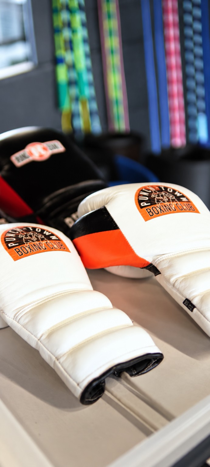 PunchTown Boxing Club gloves rest on a bench with colorful belts hanging in the background