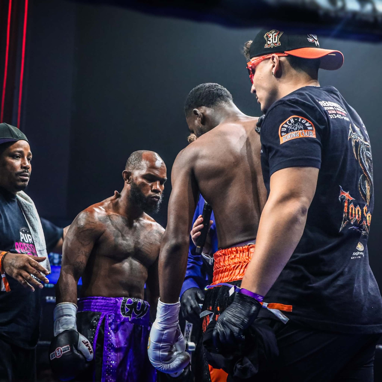 Two boxers facing each other in the ring with the PunchTown corner team nearby