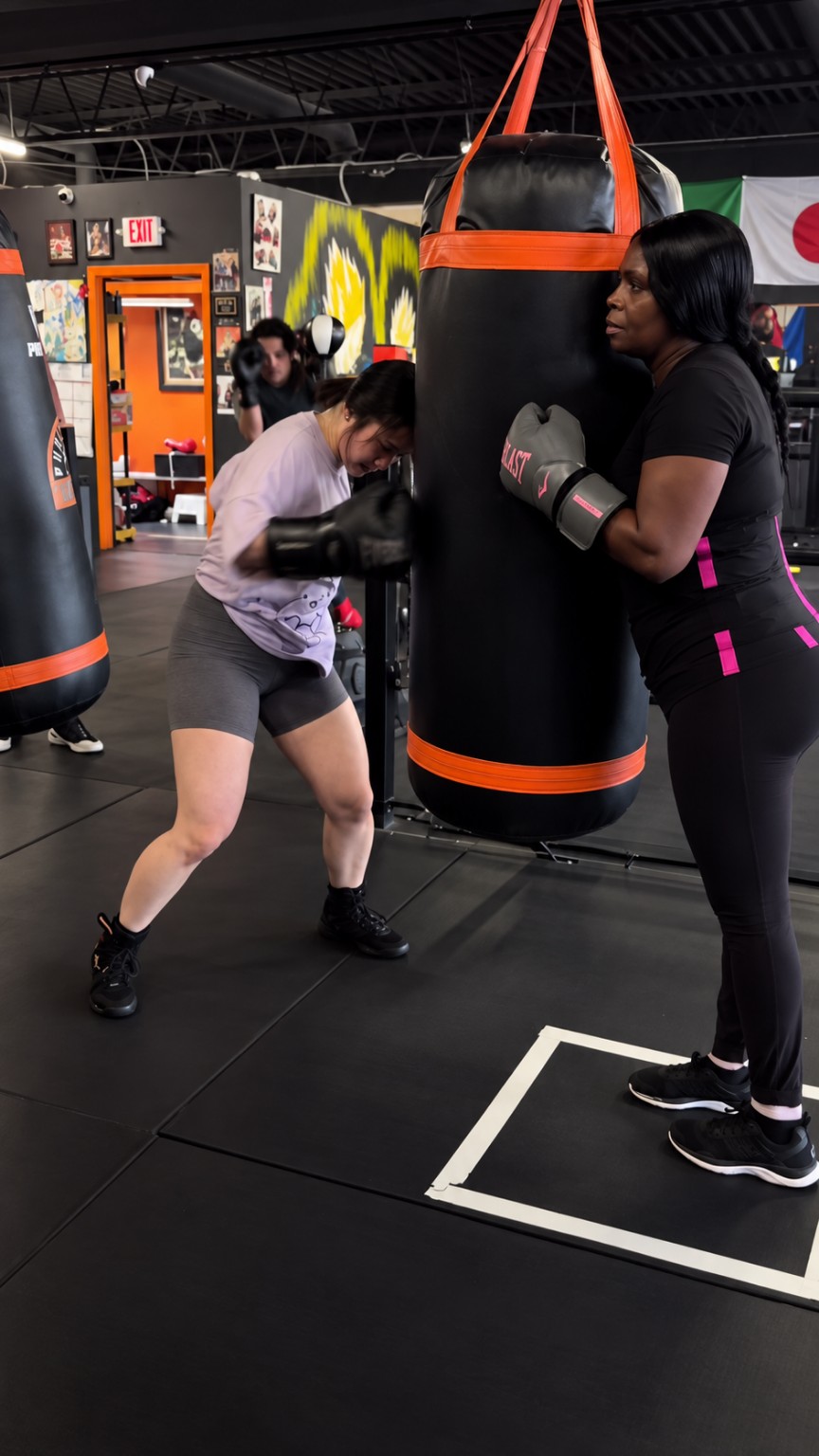 Two women training together on a heavy bag during a boxing session