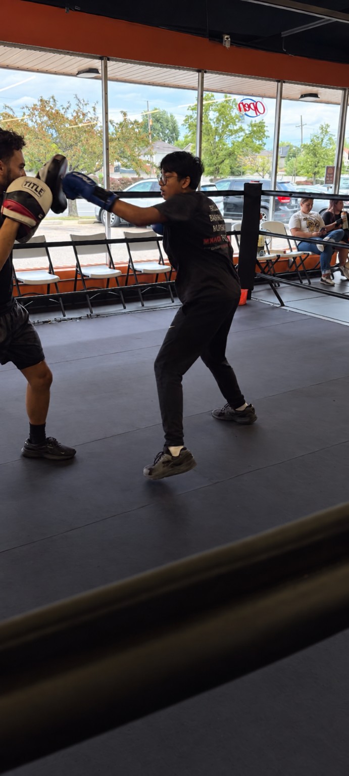 A young boxer practices punches on focus mitts inside the ring