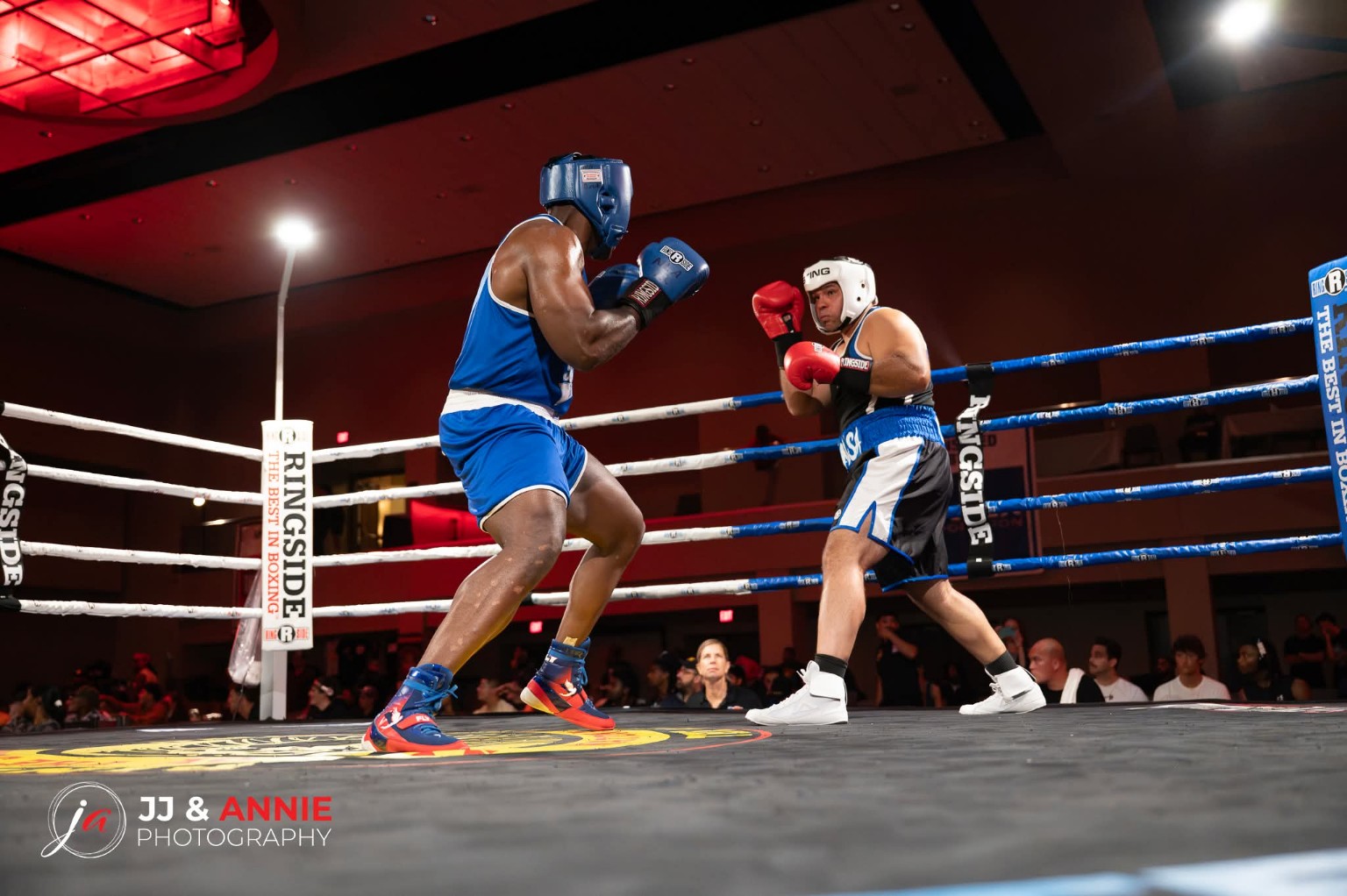 Two amateur boxers square off at center ring, one in blue and one in black and blue