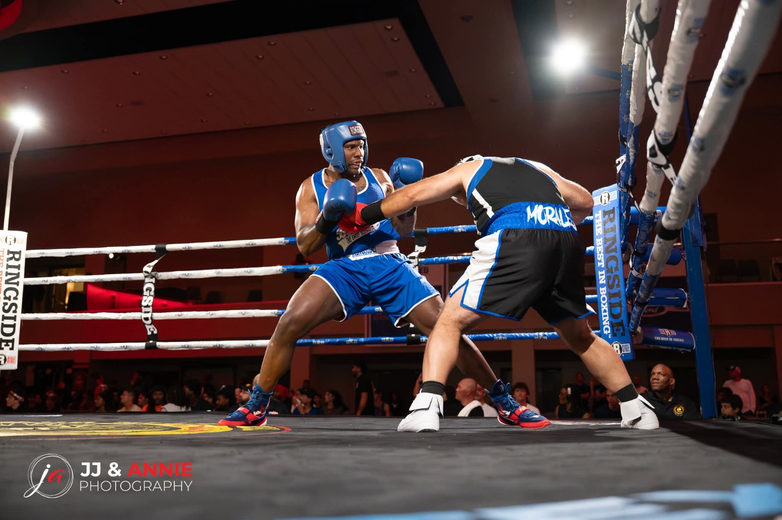 An amateur boxer in blue counters as his opponent leans forward near the corner ropes