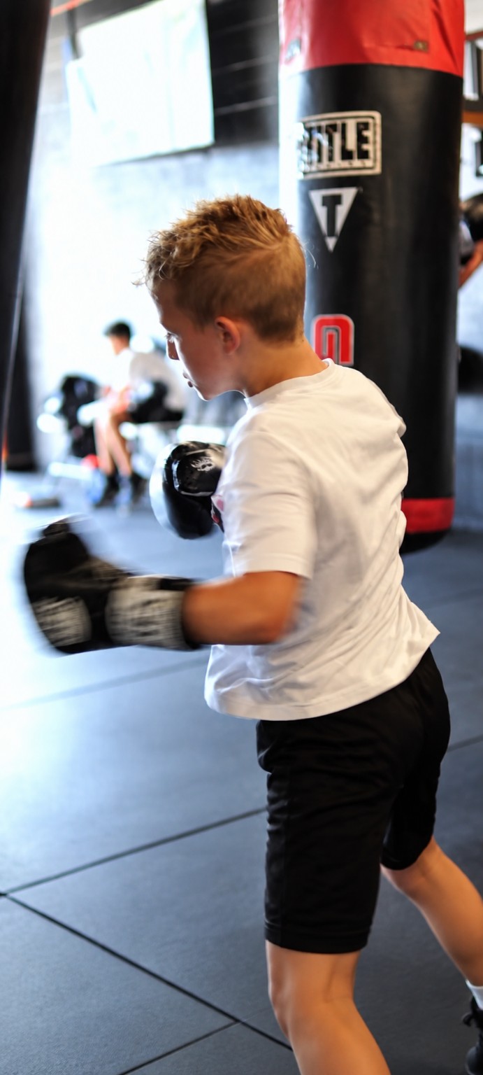 A young boxer in gloves works the heavy bag during a youth boxing session at PunchTown