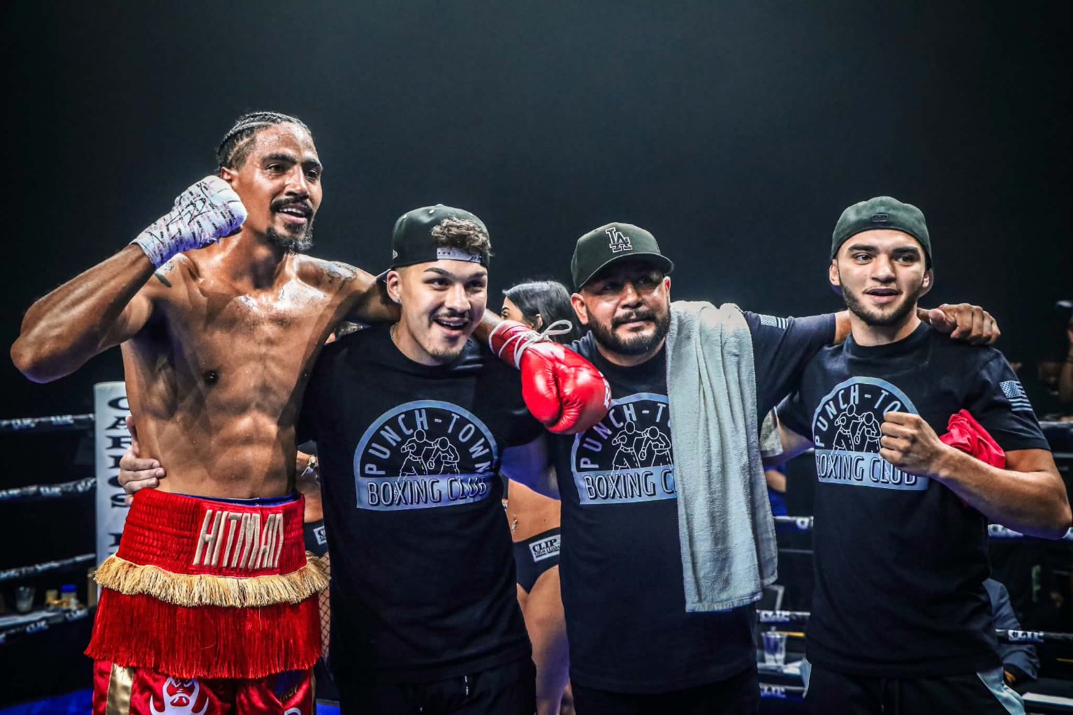 A boxer in red shorts celebrating in the ring with three teammates wearing PunchTown Boxing Club shirts