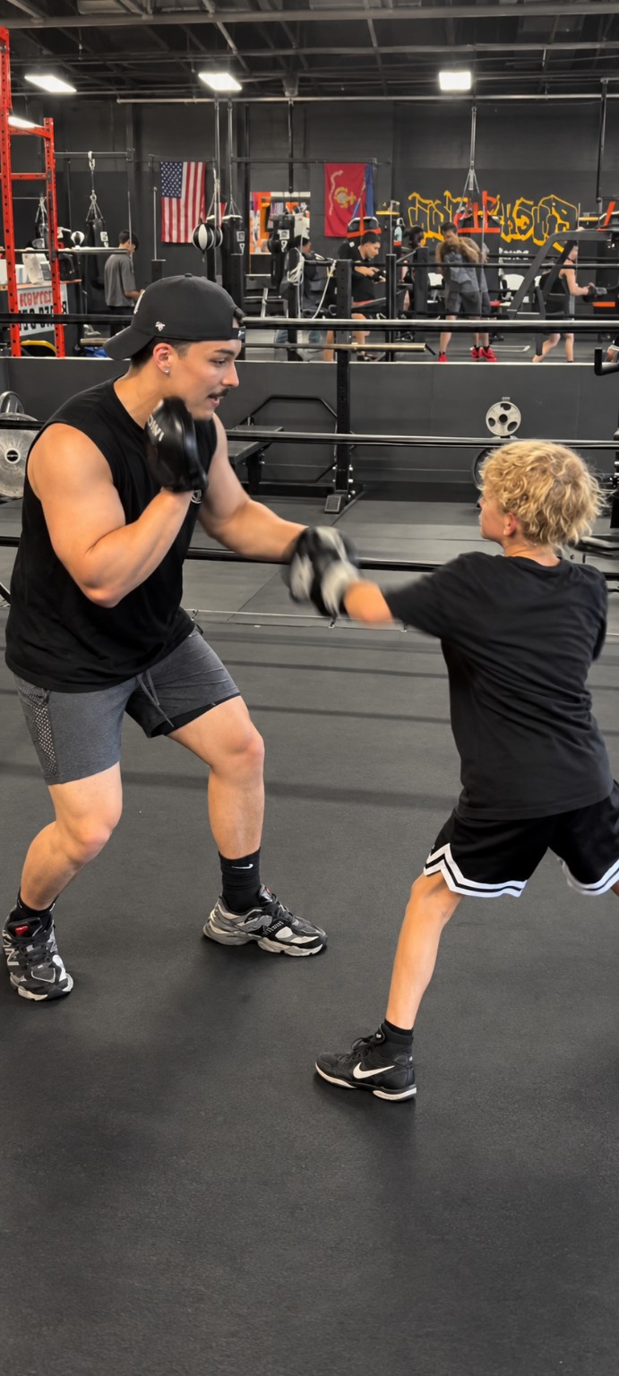 Coach guiding a young boxer through one-on-one mitt work at PunchTown.