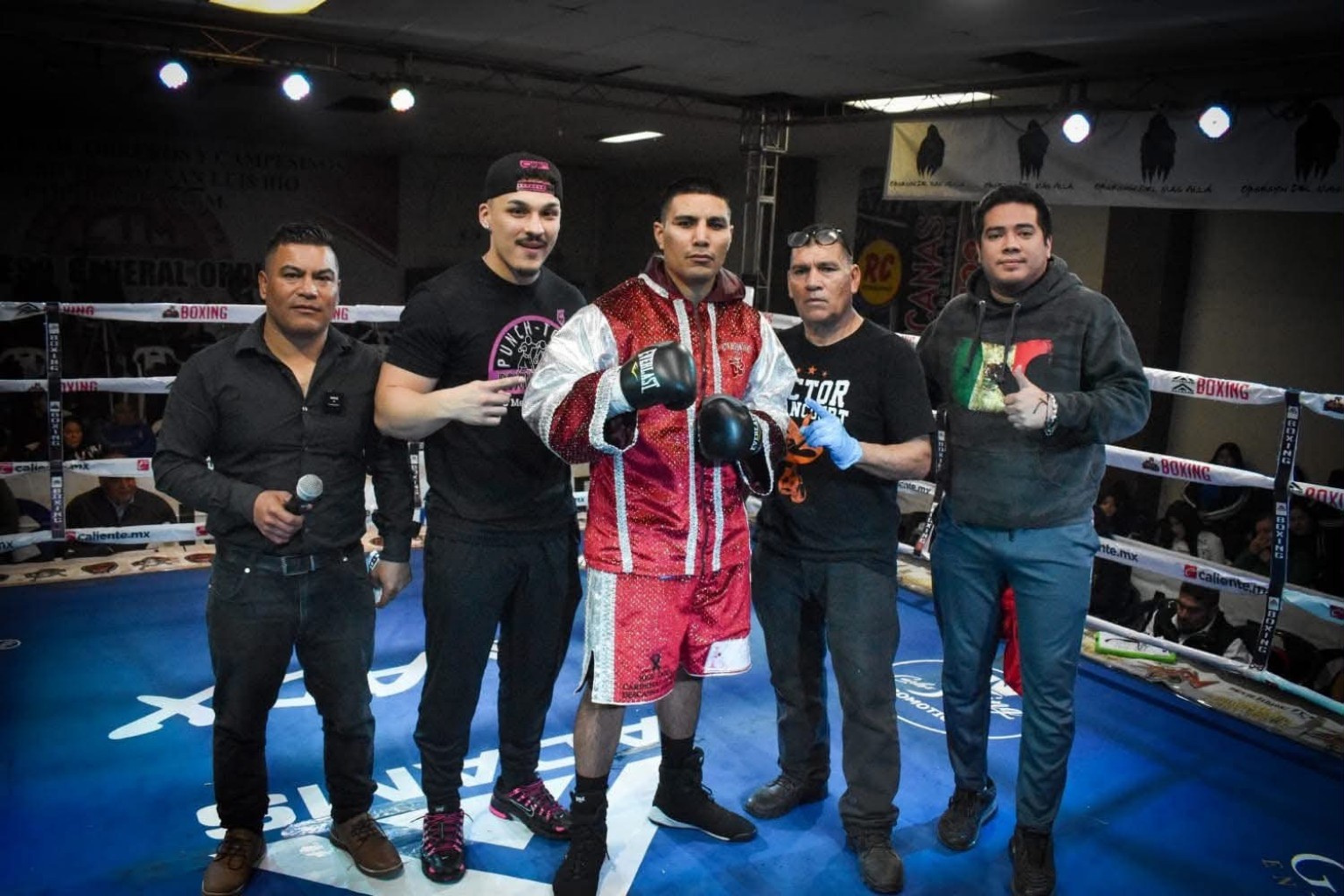 A boxer in a red and white robe standing in the ring with his corner team before a fight