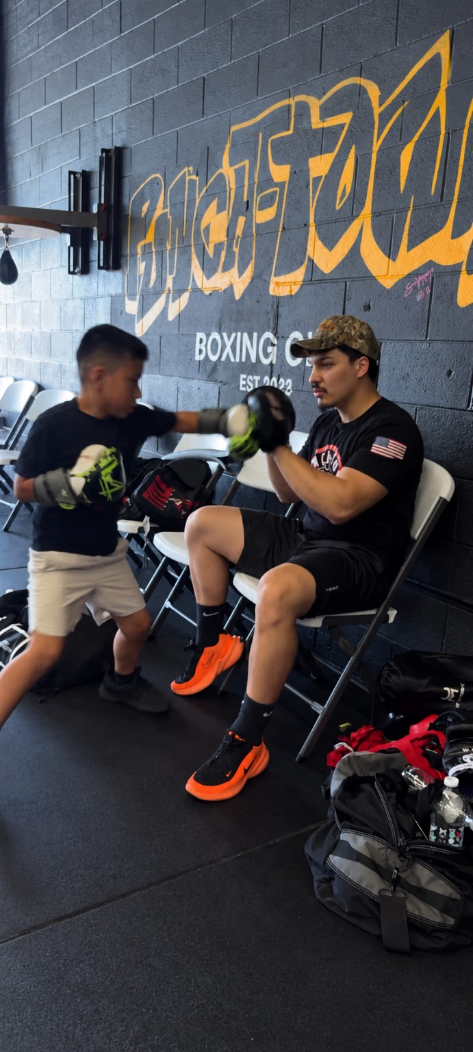 One-on-one pad work between coach and young boxer in front of the PunchTown wall.