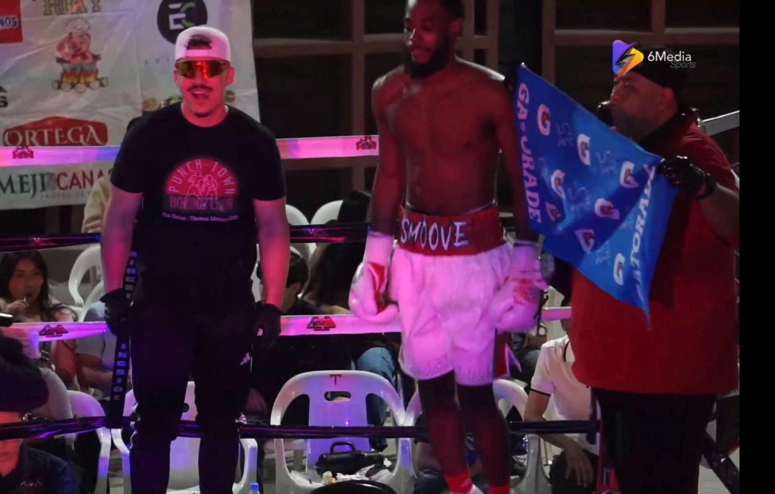 A boxer wearing white shorts with 'SMOOVE' on the waistband entering the ring with his corner team