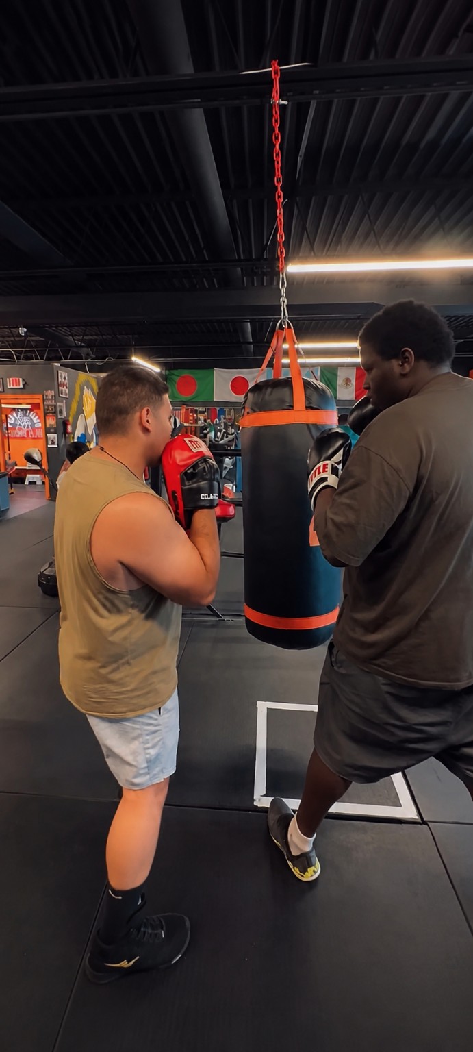 Coach guiding a boxer through heavy-bag work during one-on-one training.
